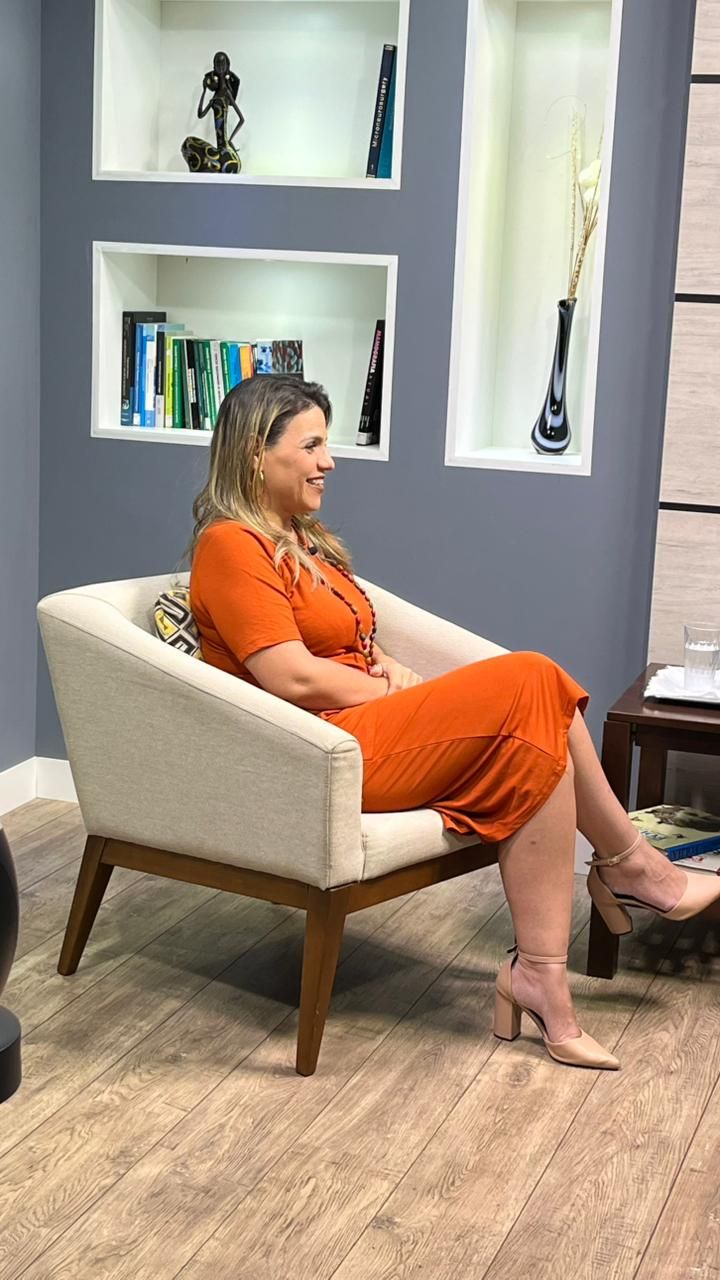 Any Marielli sentada em uma poltrona durante uma entrevista
